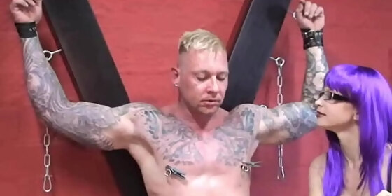 clamps on the nipples of the muscular devotee and the paddle on the ass of a sexy dominatrix in boots